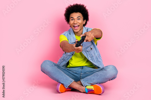 Full length photo of overjoyed excited glad man wear stylish clothes sitting playstation game isolated on pink color background photo