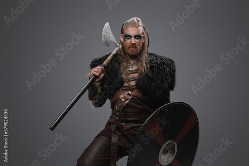 Studio shot of fearful nordic barbarian with axe with shield dressed in black fur.