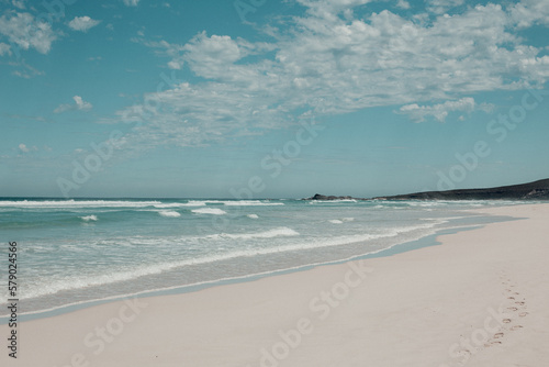 Footprints in white sand on the shore of clear water at the beach photo