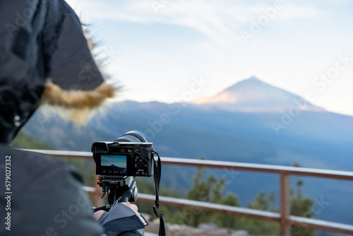 Cámara de fotografías mirrorless montada en trípode con un joven operador mirando los resultados de sus fotos y lleva una chaqueta de invierno photo