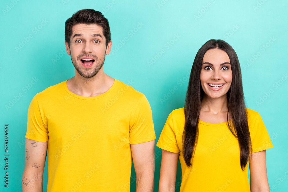 Photo of funny couple surprised good news promotion new delivery service wear empty space chest logo t-shirt isolated on aquamarine color background Photo of funny couple surprised good news promotion new delivery service wear empty space chest logo t-shirt isolated on aquamarine color background