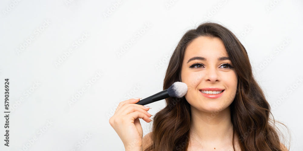 Banner with smiling young woman holding a cosmetic brush near her face. Makeup artist applying face powder. Banner with smiling young woman holding a cosmetic brush near her face. Makeup artist applying face powder.