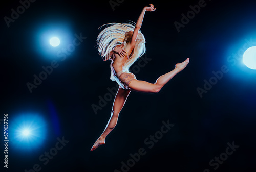 Fototapeta Naklejka Na Ścianę i Meble -  Young blond woman jumping on dark background with blue lights
