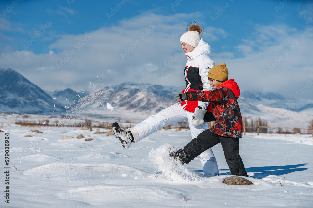 Young woman with child walking in snow on mountains background at sunny day