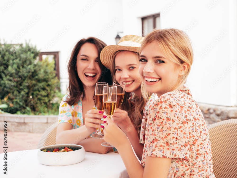 Three young beautiful smiling hipster female celebrating. Carefree women posing at summer terrace veranda cafe in the street.Positive models drinking champagne. Enjoying their vacation. Talking Three young beautiful smiling hipster female celebrating. Carefree women posing at summer terrace veranda cafe in the street.Positive models drinking champagne. Enjoying their vacation. Talking