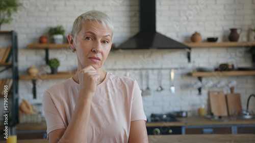 Slika na platnu Elderly pensive woman thoughtfully at idea hold hand to chin with puzzled facial