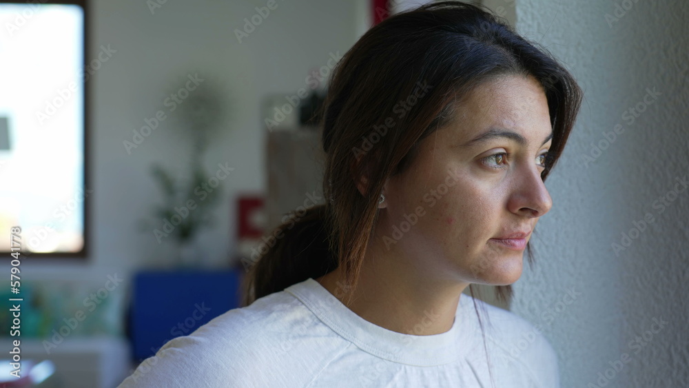 One pensive woman standing by window in contemplation looking out. A thoughtful adult female person thinking about life. 30s age One pensive woman standing by window in contemplation looking out. A thoughtful adult female person thinking about life. 30s age