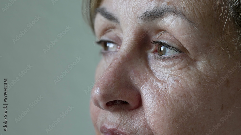 Fototapeta premium One contemplative mature woman close up eyes staring at horizon in meditation. An older pensive senior female person in 70s. Thoughtful expression