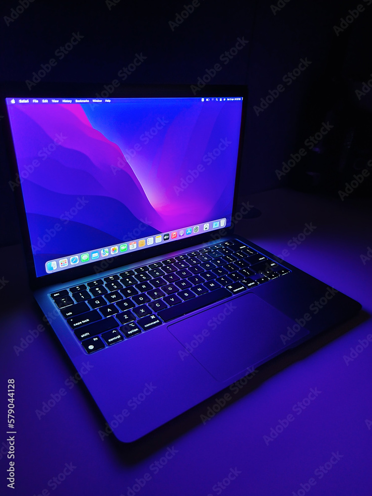 Stockfoto Apple MacBook Air M1 Chip Laptop with lid open on a table lit  with colorful purple and blue desktop screen wallpaper in a dark room on  March 8, 2023 Dubai, United
