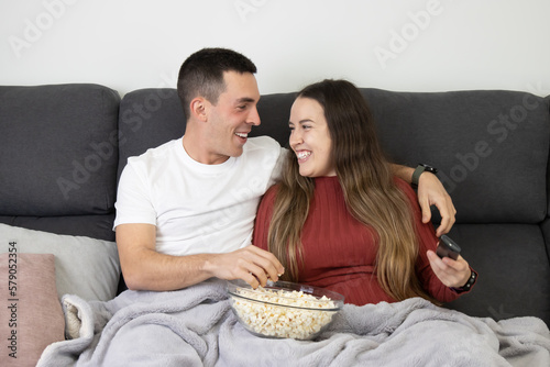 Couple lying on the sofa eating popcorn while watching TV