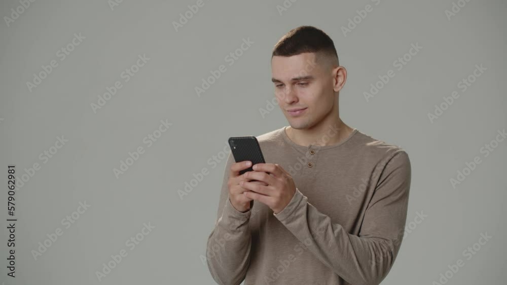 Smiling man surfs internet on smartphone. A man standing on a white background holds a smartphone in his hands. Smiling man surfs internet on smartphone. A man standing on a white background holds a smartphone in his hands.