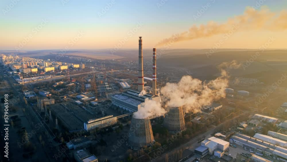 Aerial drone view of thermal power plant in Chisinau at sunrise, Moldova. View of pipes with felling steam, infrastructure around, cityscape on the background