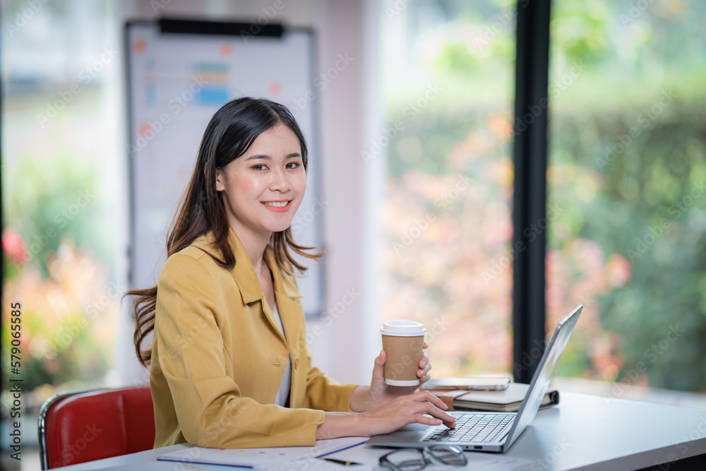 Sharing good business news. Attractive young businesswoman talking on the mobile phone and smiling while sitting at her working place in office and looking at laptop.