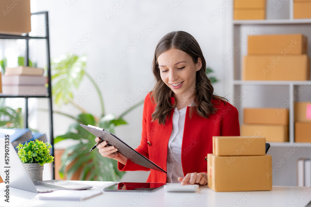 Female ecommerce business owner prepares package box for customer and delivery check balance. SME. Female ecommerce business owner prepares package box for customer and delivery check balance. SME.