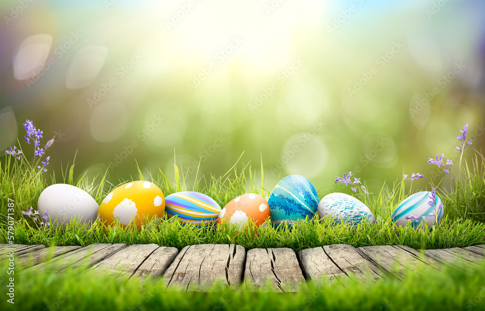 A collection of painted easter eggs celebrating a Happy Easter on a spring day with green grass meadow background with copy space and a rustic woodern bench to display products.