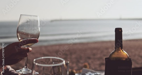 Group of friends cheering with glasses of wine and beer at the ocean beach restaurant in summer. Unrecognizable people celebrating vacation party, having dinner together in a cozy bar by the sea