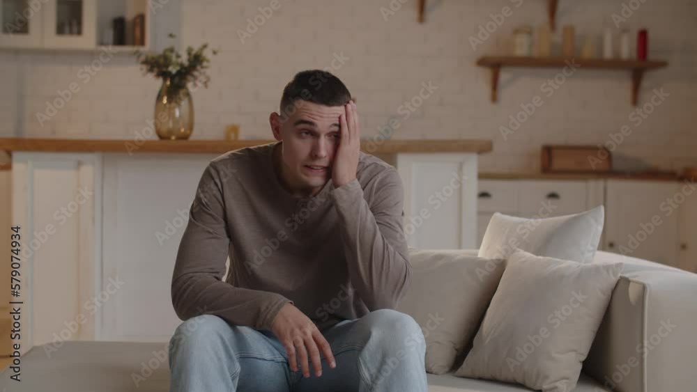 A worried man clutches his head while sitting on the couch. The short-haired man clutches his head and sighs in anticipation of bad news. A worried man clutches his head while sitting on the couch. The short-haired man clutches his head and sighs in anticipation of bad news.