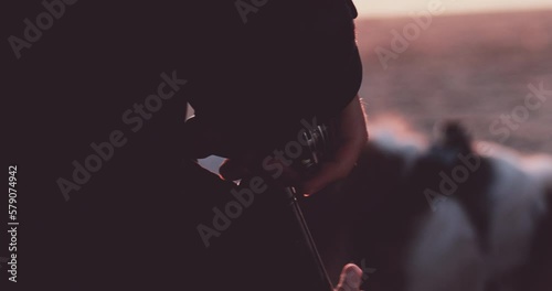 Person opens a bottle of wine with a corkscrew on ocean beach at sunset. Romantic dinner picnic near the sea, unrecognizable man preparing drinks. Summer vacation memories. tranquil relaxing moment.  photo