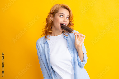 Young woman eat ice creams with chocolate glaze on yellow background. Funny redhead woman with ice cream.