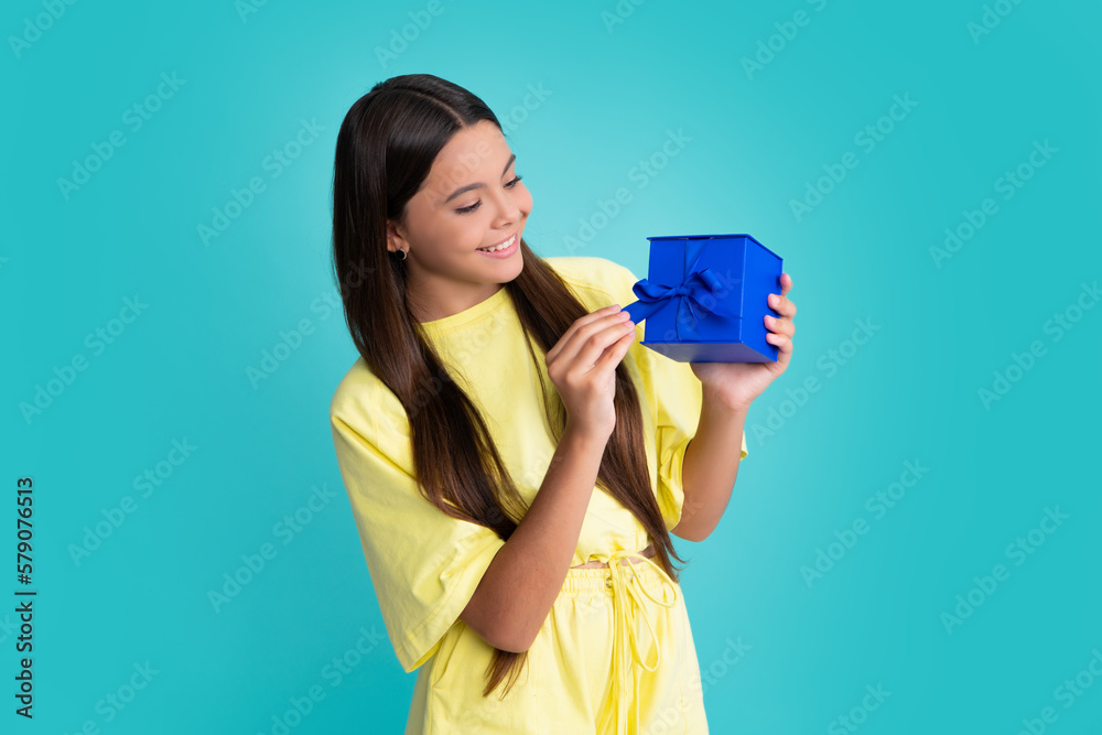 Teenager child holding gift box on blue isolated background. Gift for kids birthday. Christmas or New Year present box. Happy girl face, positive and smiling emotions. Teenager child holding gift box on blue isolated background. Gift for kids birthday. Christmas or New Year present box. Happy girl face, positive and smiling emotions.