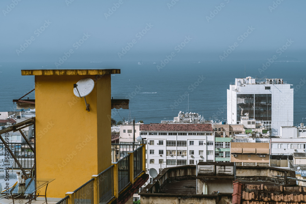 From a highrise apartment in Rio de Janeiro, Brazil, the view shows a serene sea and surrounding buildings, with some appearing old and dilapidated