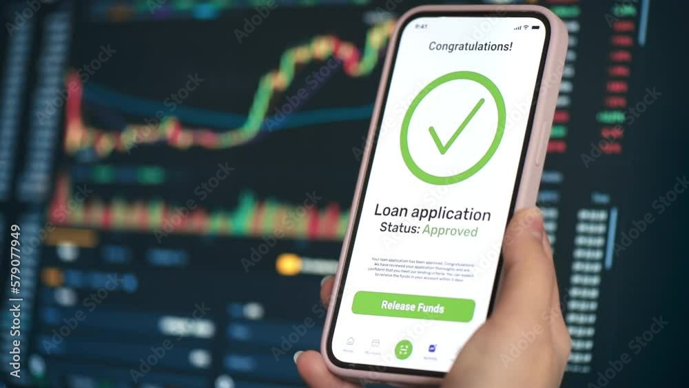 Close view of a person holding smartphone with opened loan application, loan approved info. Stock charts on the background