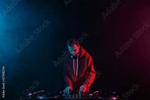 Club DJ mixing vinyl records with sound mixer on a party in night club. Young adult male person performing as a disc jockey