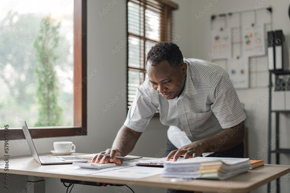 Happy African man using laptop computer and calculator for calculating invoice at home