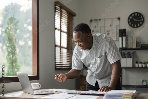 Happy African man using laptop computer and calculator for calculating invoice at home