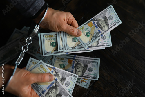 Hands of a fraudster with handcuffs on a background of us dollars. Fraud, cyber crime concept. Arrest of an entrepreneur in the workplace.