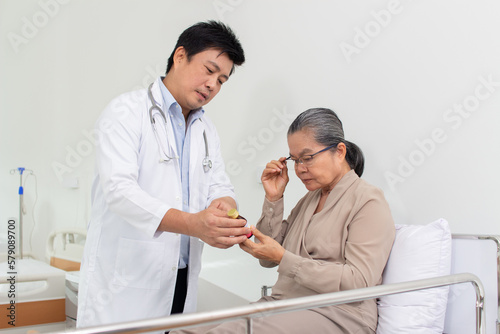 Asian male doctor explaining medicine to elderly female patient in hospital.