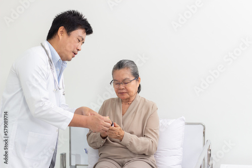Asian male doctor explaining medicine to elderly female patient in hospital.