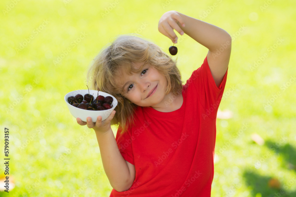 Cute little boy in red tshirt eating cherries, making funny faces and