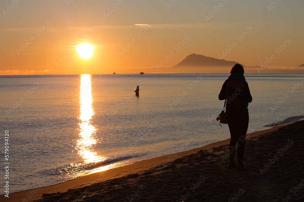 Amanecer en la Playa de Miramar, Valencia, con siluetas de pescador y mujer paseando por la playa