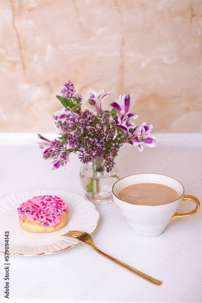 Coffee cup and sweet strawberry donut on golden plate with flower bouquet
Coffee cup and sweet strawberry donut on golden plate with flower bouquet