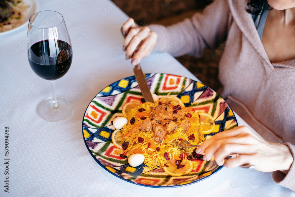 High angle view of the unrecognizable woman eating pilaf with meat ad drinking red wine