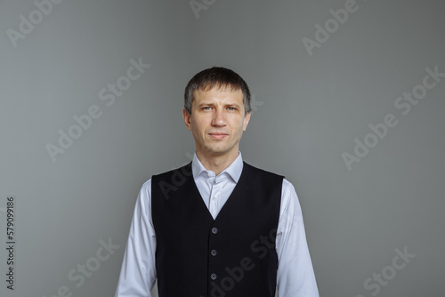 A man in a white shirt and a black vest on a gray background
