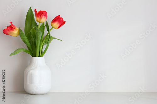 Vase with tulips on the table in the room against the wall. Happy Mothers Day, International Womens Day greeting card design.
