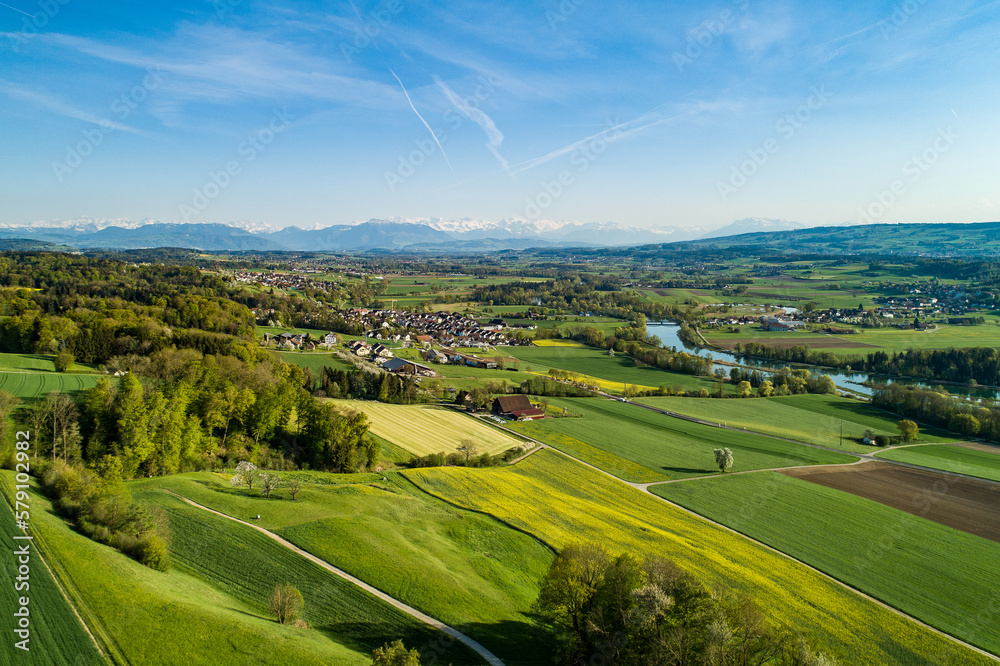 Panoramablick über die Reussebene und den Flachsee in die Alpen. Ein Mosaik aus sattgrünen Wiesen, Rapsfeldern und Ackerflächen zieht sich bis zu den Voralpen und Bergen am Horizont..
