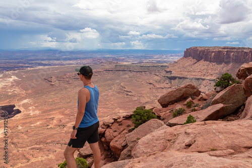 Man with scenic view on Split Mountain Canyon seen from Grand View Point Overlook near Moab, Island in the Sky District, Canyonlands National Park, San Juan County, Utah, USA. Dark clouds accumulating © Chris