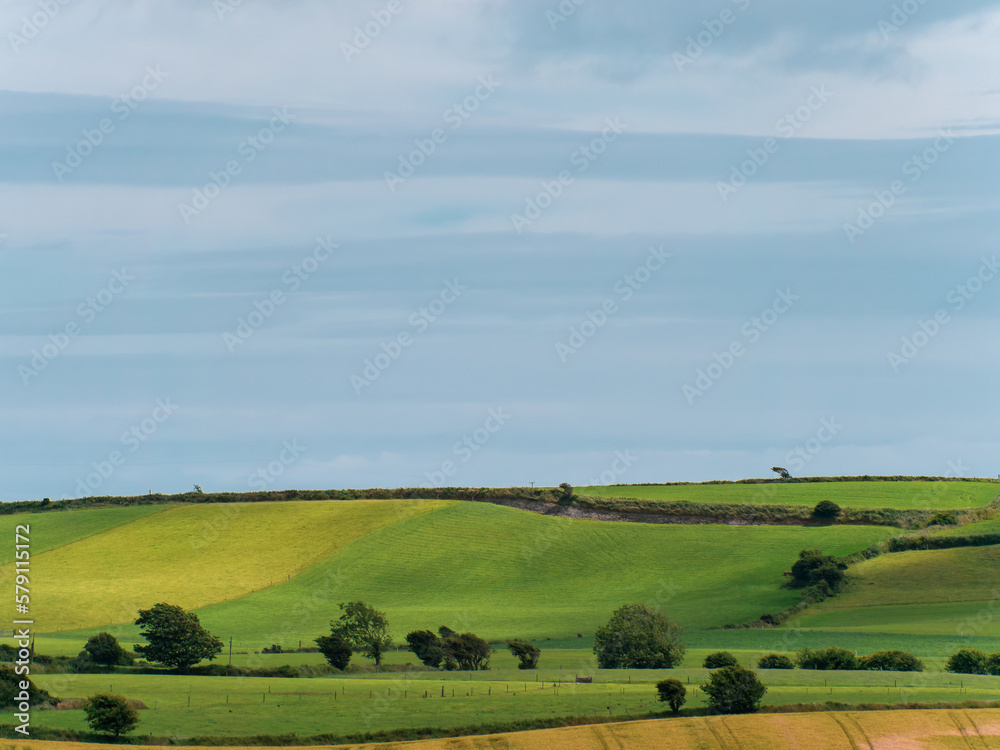 Picturesque agricultural landscape. Green hills, blue sky. Hilly terrain in the Ireland, nature.