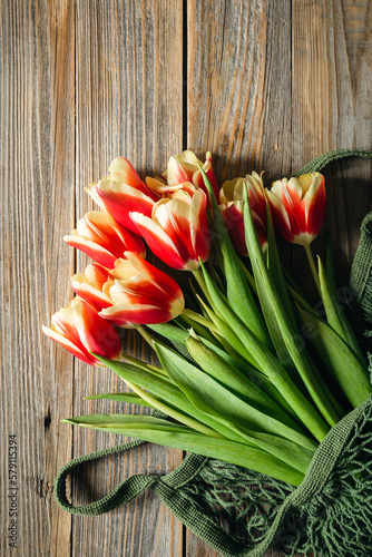 Bouquet of fresh tulips in a string bag on a wooden background, top view, concept of mother's day, women's day, spring background with a bouquet of flowers, rustic style.
