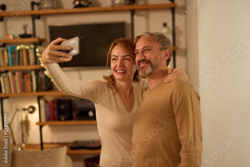 Cheerful mature couple taking selfie with smart phone at home