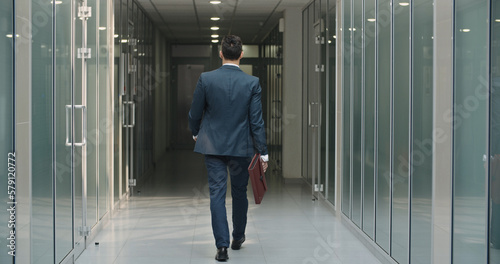 Rear view of classy asian businessman. The man holding business handbag with office formal suit walking in office building. A student walks down the hall during a break at a business university