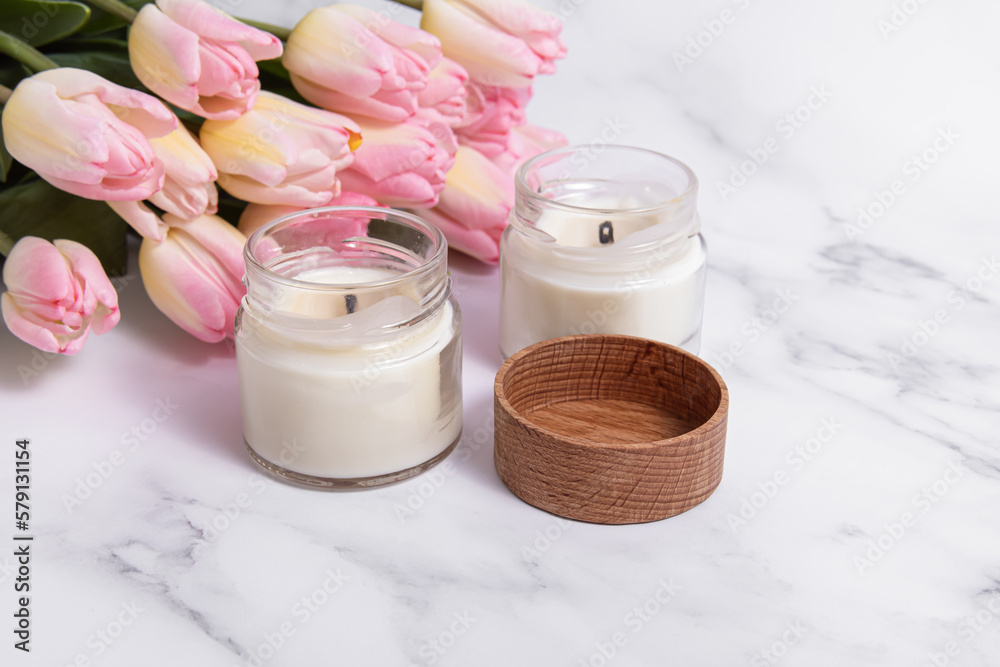 Two scented candles and pink tulips on marble background. Candles in glass Two scented candles and pink tulips on marble background. Candles in glass