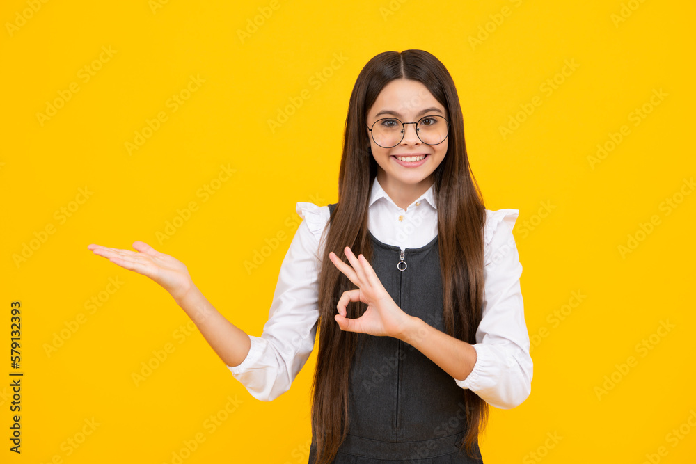 Portrait of cute teenager child girl pointing hand showing adverts with copy space over yellow background. Happy girl face, positive and smiling emotions. Portrait of cute teenager child girl pointing hand showing adverts with copy space over yellow background. Happy girl face, positive and smiling emotions.