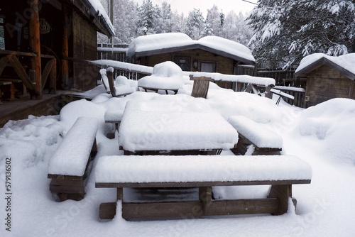 Snow covered tables and benches outside by wooden house in countryside