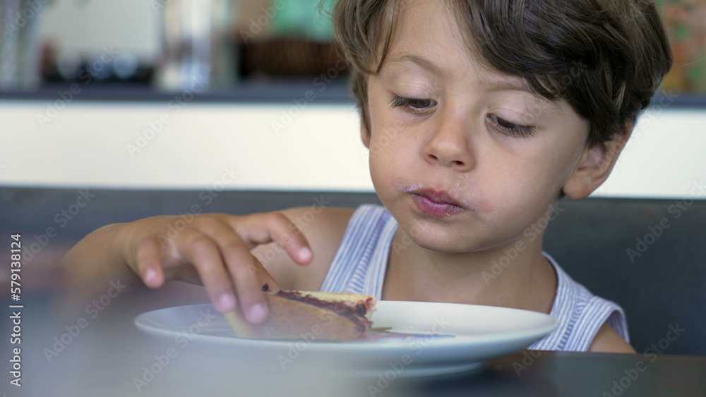 One small boy seated at breakfast table chewing food in front of bread with jelly