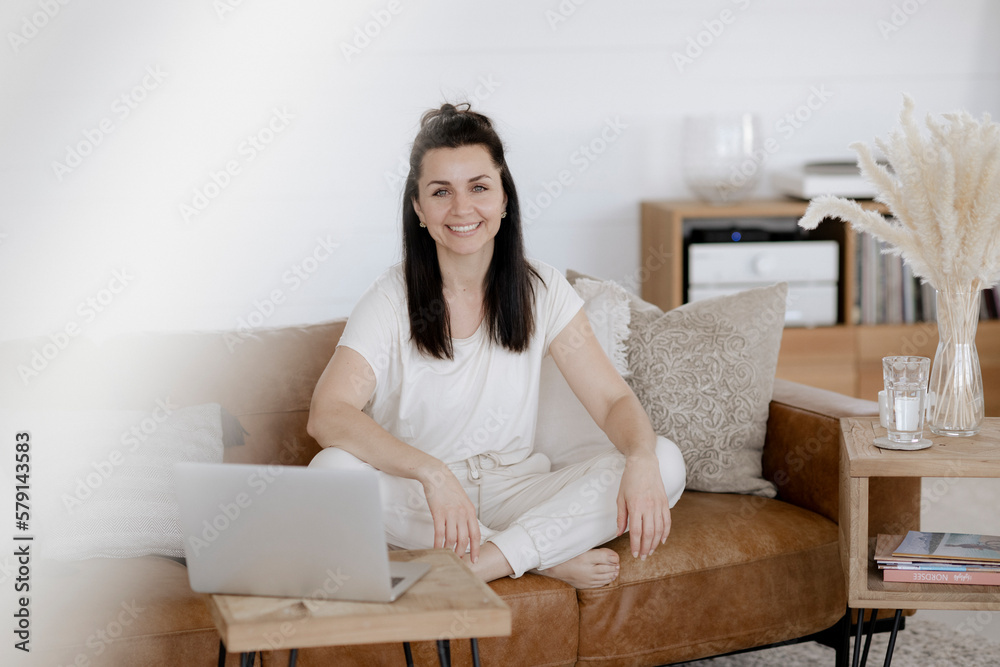 Dunkelhaarige Frau, 35+, sitzt gemütlich auf der Couch und arbeitet am Laptop Dunkelhaarige Frau, 35+, sitzt gemütlich auf der Couch und arbeitet am Laptop