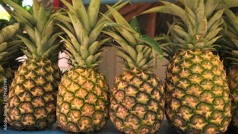 Slow motion shot of pineapples rack focus on counter of a fruit shop on the beach. Fresh fruits, juices and vitamins whole year in a tropical country. Slow motion shot of pineapples rack focus on counter of a fruit shop on the beach. Fresh fruits, juices and vitamins whole year in a tropical country.